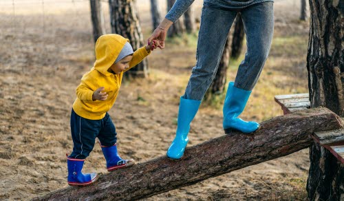 Litet barn får hjälp av vuxen att balansera på en trädstock.