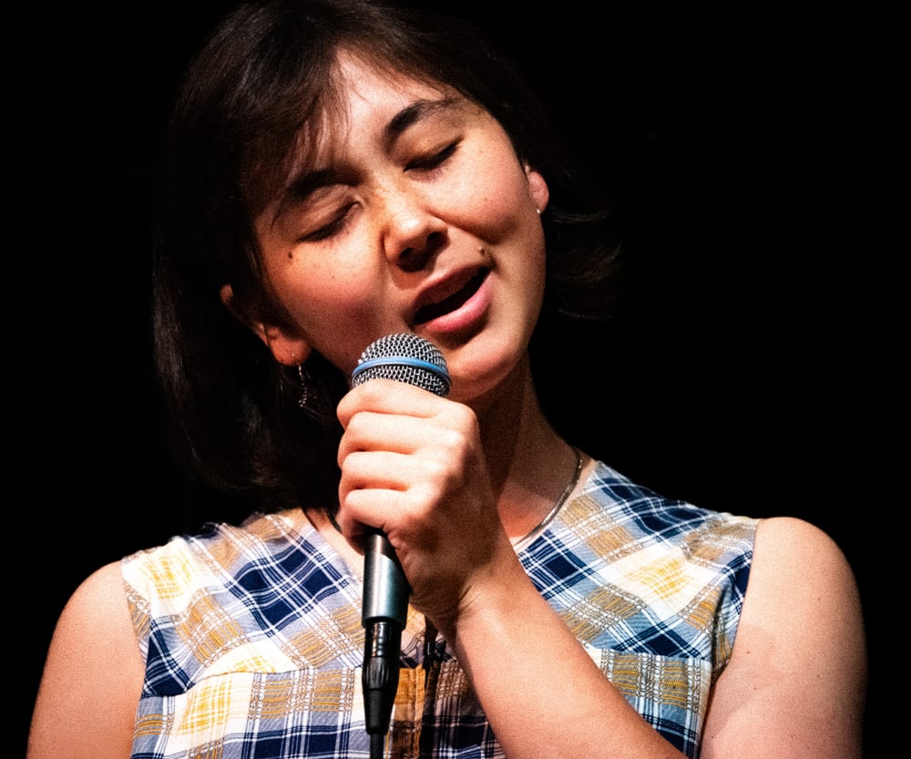 Person sjunger i en mikrofon på en scen.