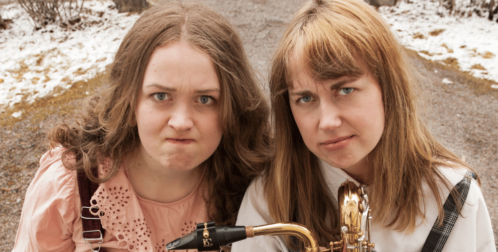 Två kvinnor står bredvid varandra och håller i en saxofon.