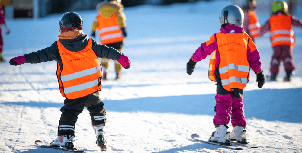 En grupp förskolebarn som åker skidor nerför en snötäckt backe.