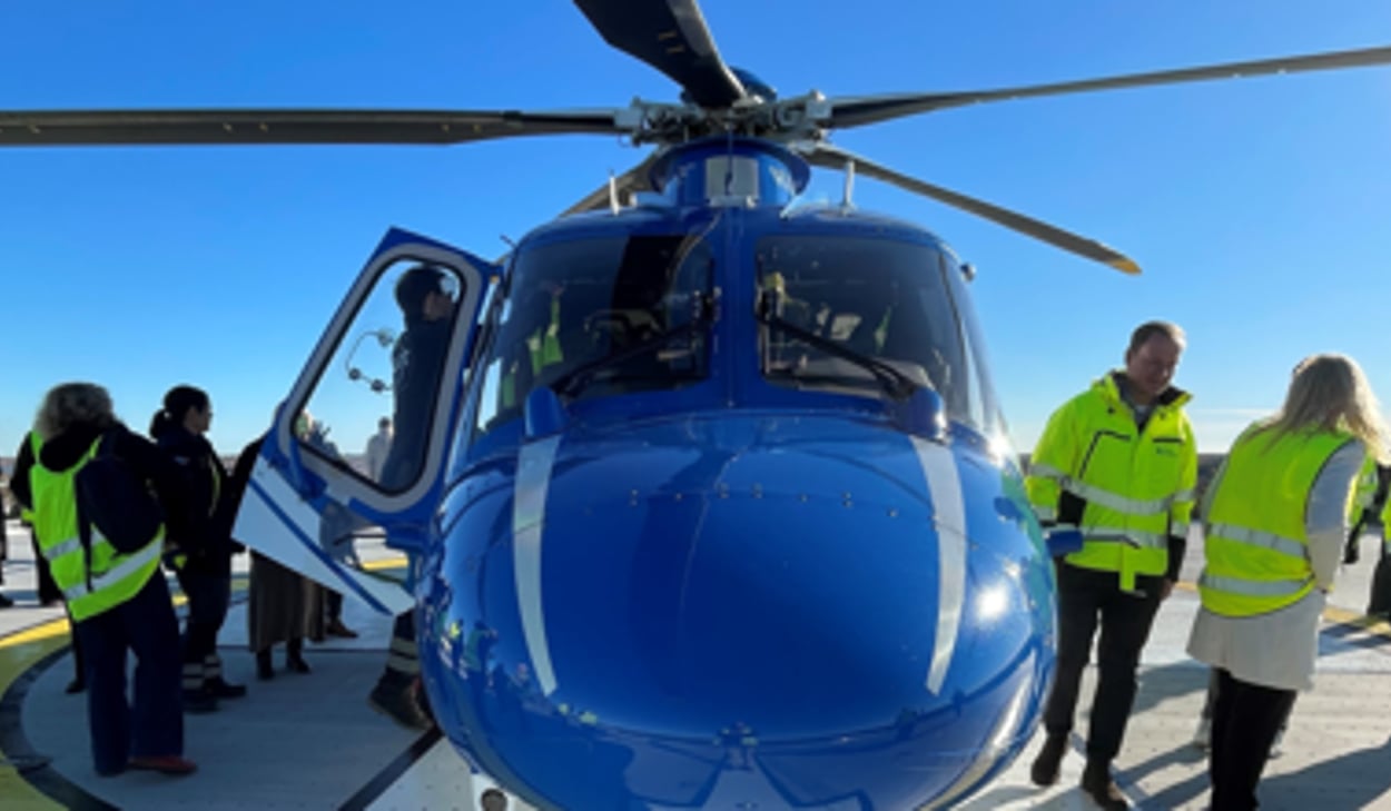En grupp människor som står runt en blå helikopter.