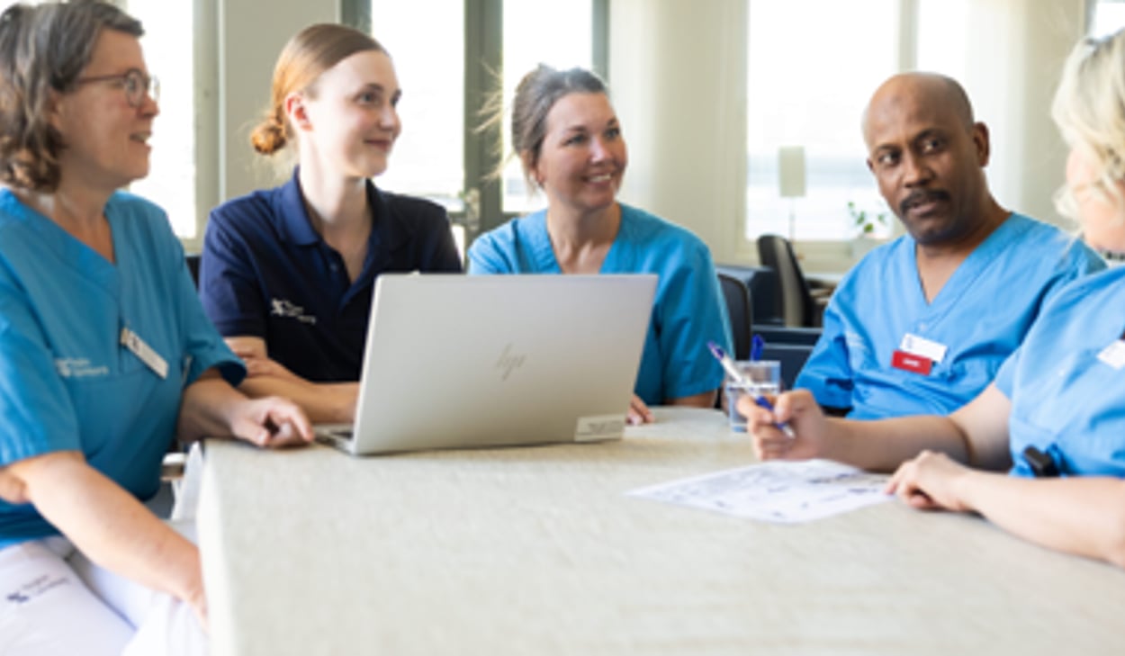 En grupp medarbetare som sitter runt en bärbar dator.