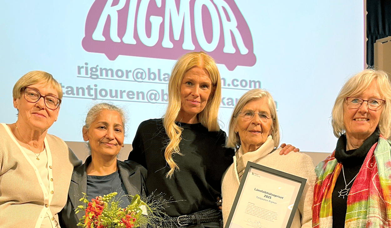 Fem personer i halvfigur står framför en skärm med ordet Rigmor. De har blommor och diplom i händerna