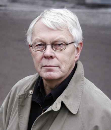 En man med vitt h&aring;r som b&auml;r en trenchcoat.