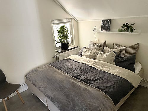 En s&auml;ng som st&aring;r i ett sovrum bredvid ett f&ouml;nster.