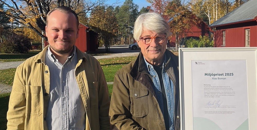 Två män står bredvid varandra i utomhusmiljö på hösten. Den ena håller i ett inramat diplom för Miljöpriset 2025.