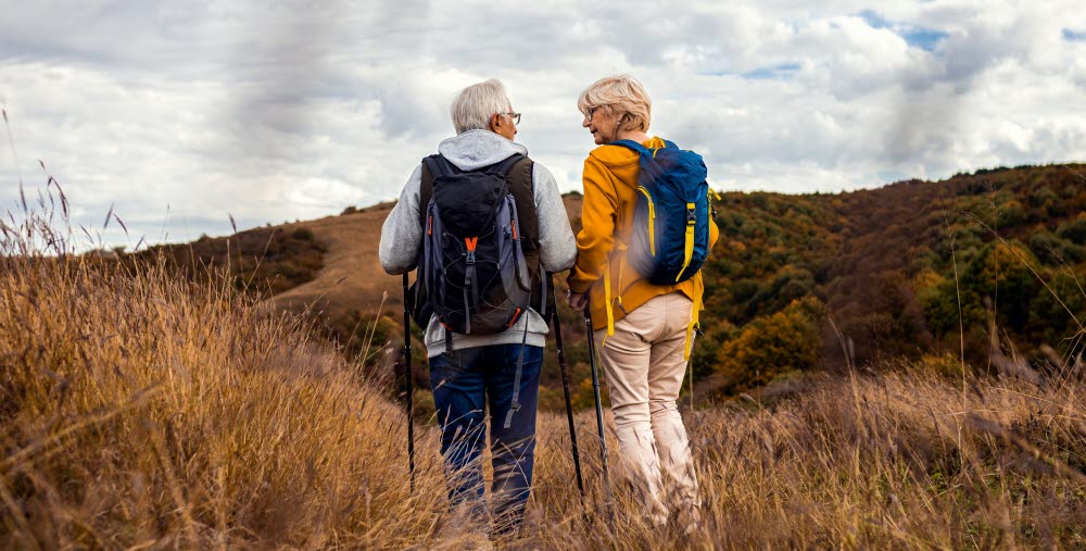 Två personer vandrar med ryggsäckar på en stig i ett öppet landskap.