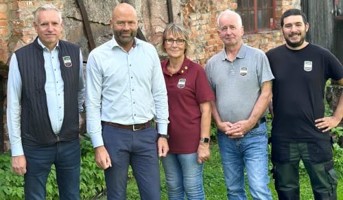 Fem personer står i helkroppsfigur framför en gammal tegelbyggnad.