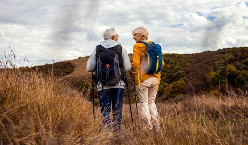 Två personer vandrar med ryggsäckar på en stig i ett öppet landskap.
