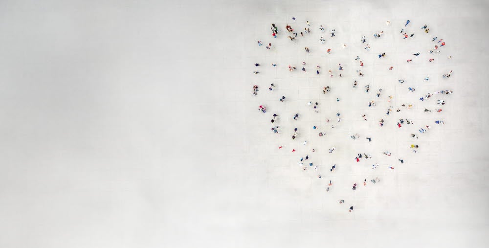 Människor står utspridda så att de tillsammans bildar formen av ett hjärta på en stor öppen yta, sedd uppifrån.