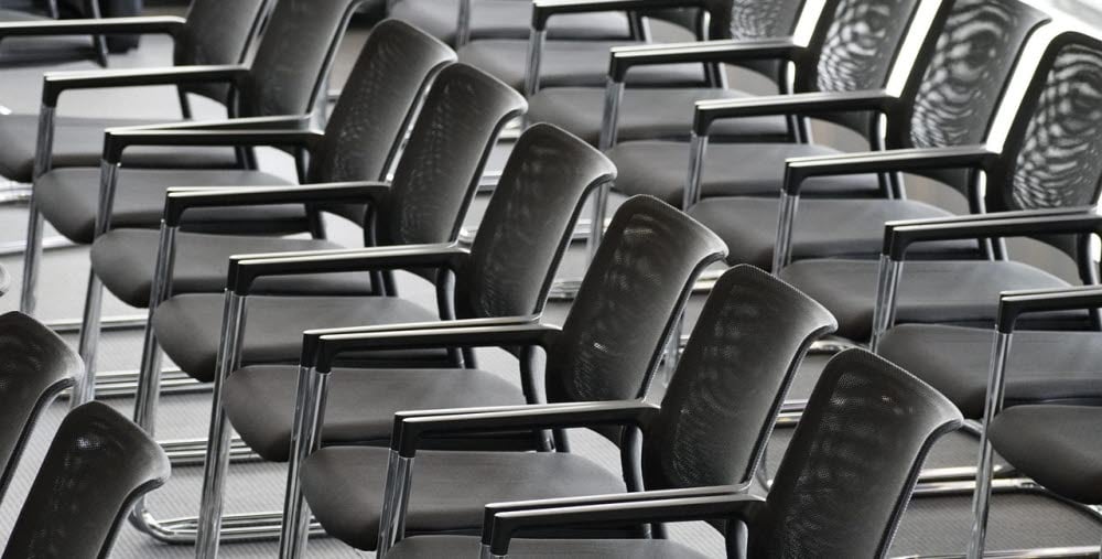 Rader av tomma svarta stolar i ett konferensrum.